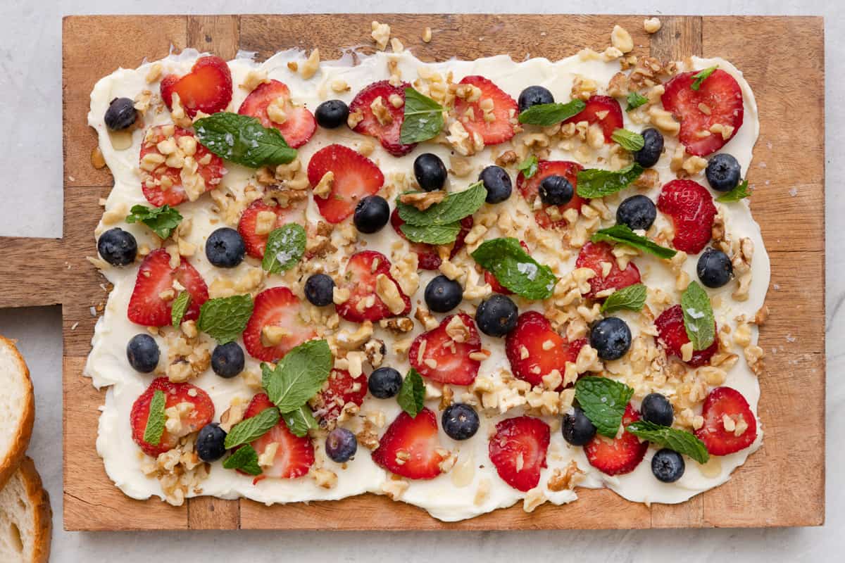 Butter board topped with sliced strawberries, blueberries, nuts, and fresh mint leaves.