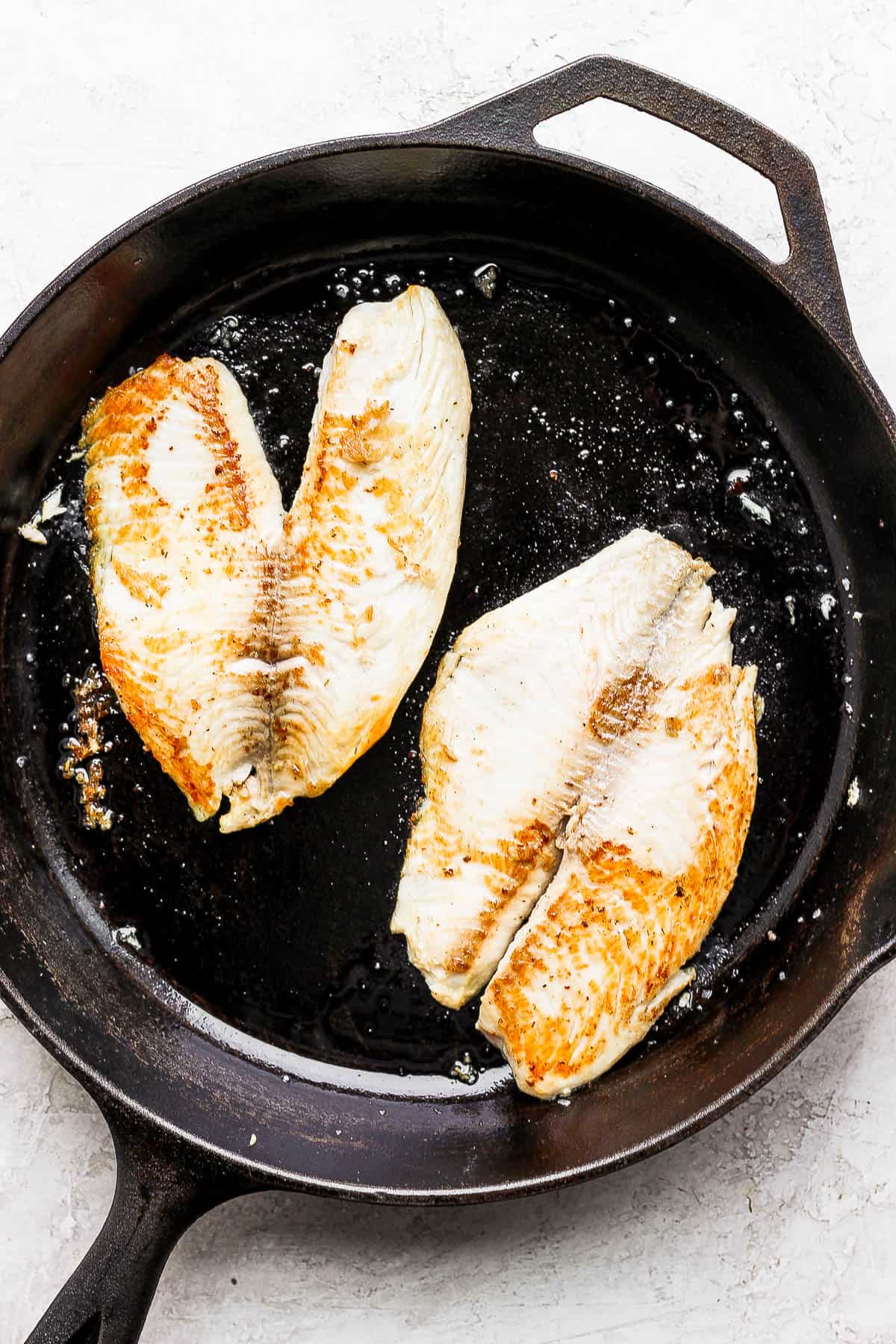 2 fish filets grilled in a cast iron skillet.