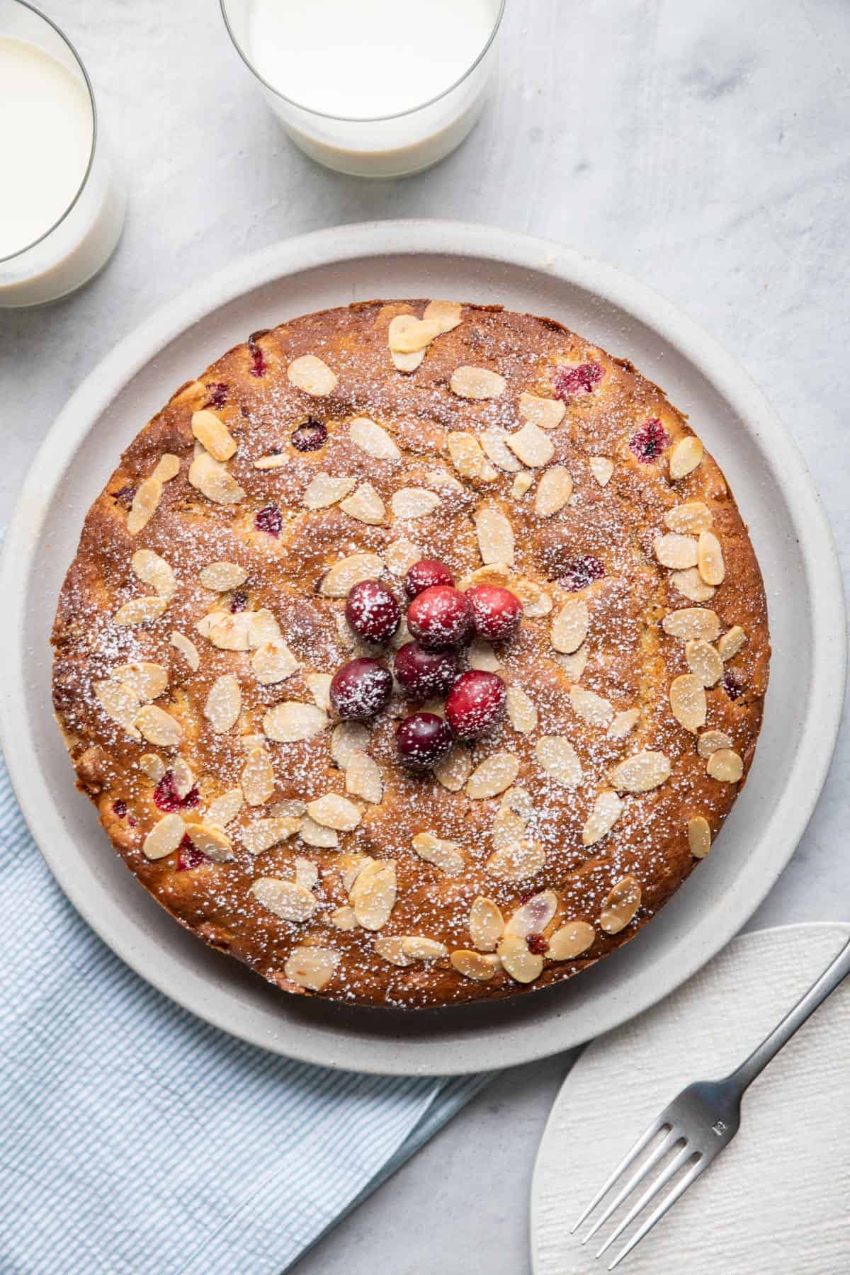 Craberry Cake with almonds on a plate with fresh cranberries on top and dusted with powdered sugar.