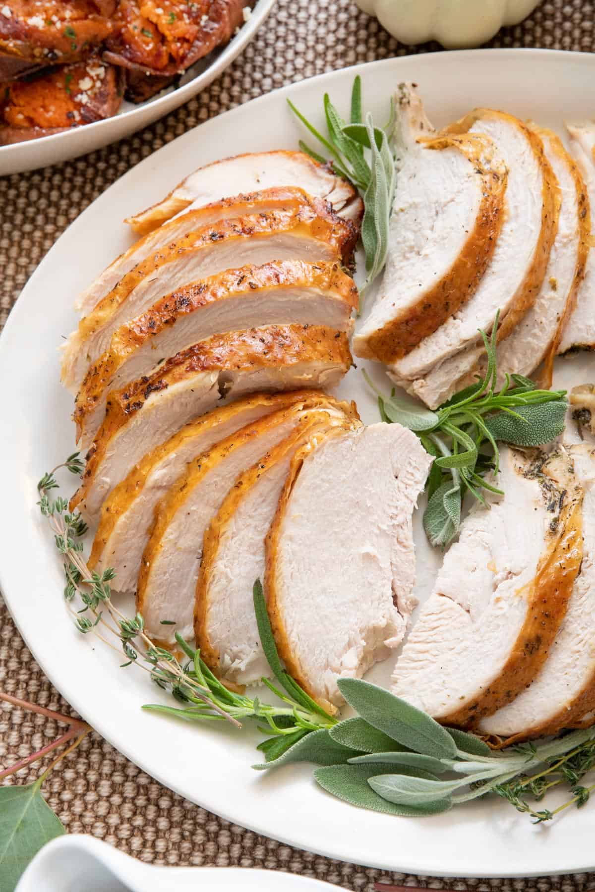 Slice turkey breast fanned out on a platter with fresh herbs.