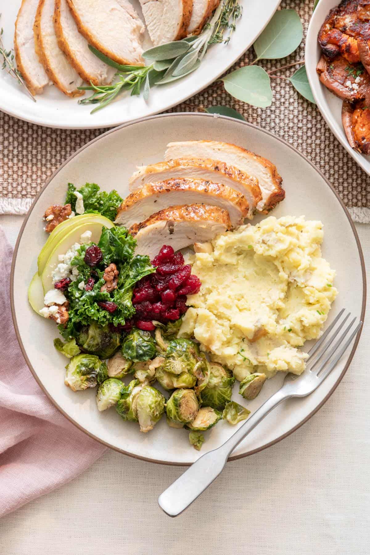 Plate with turkey, pear slad, cranberry sauce, mashed potatoes, and brussels sprouts with fork.