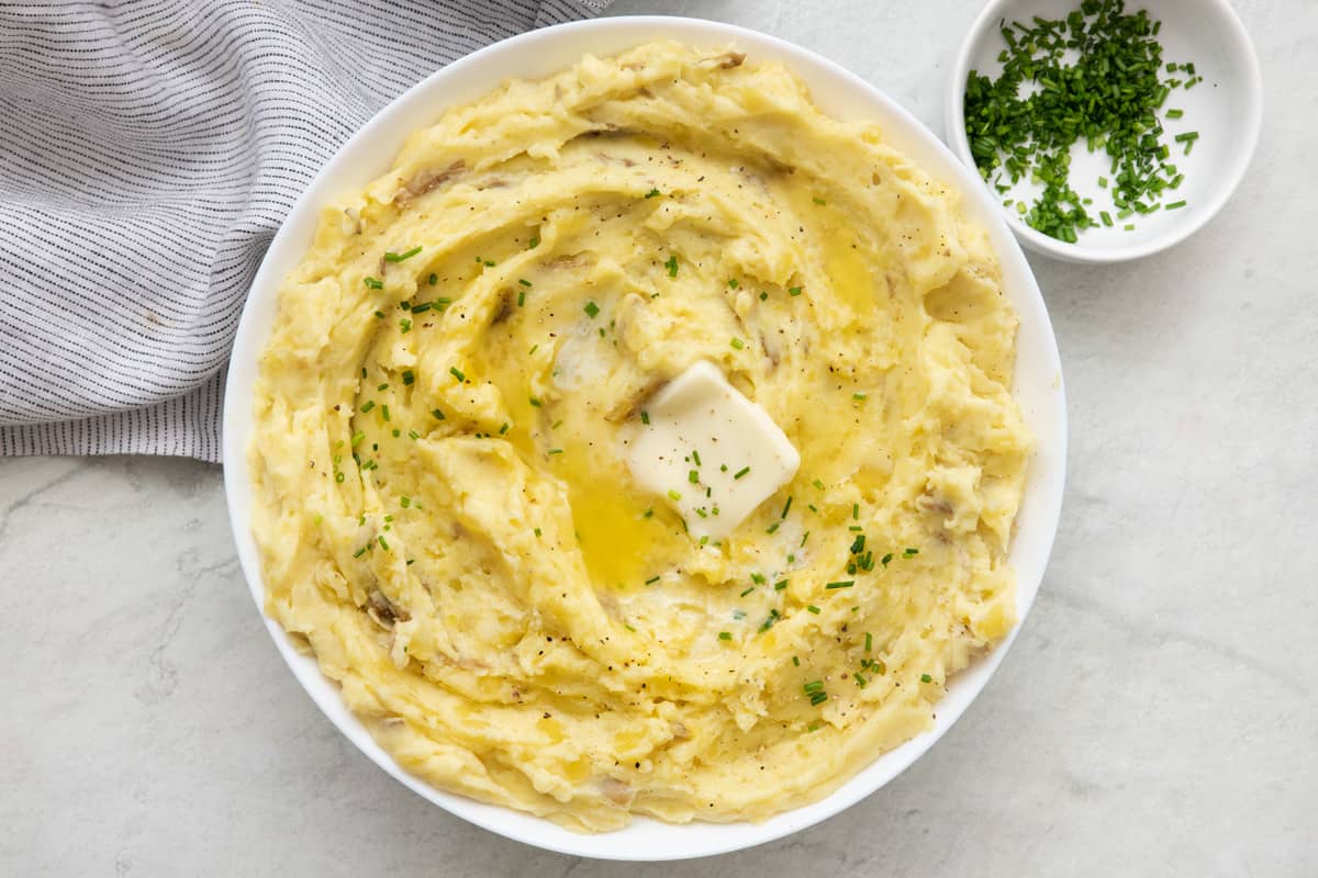 Large serving dish of garlic mashed potatoes topped with butter and herbs.
