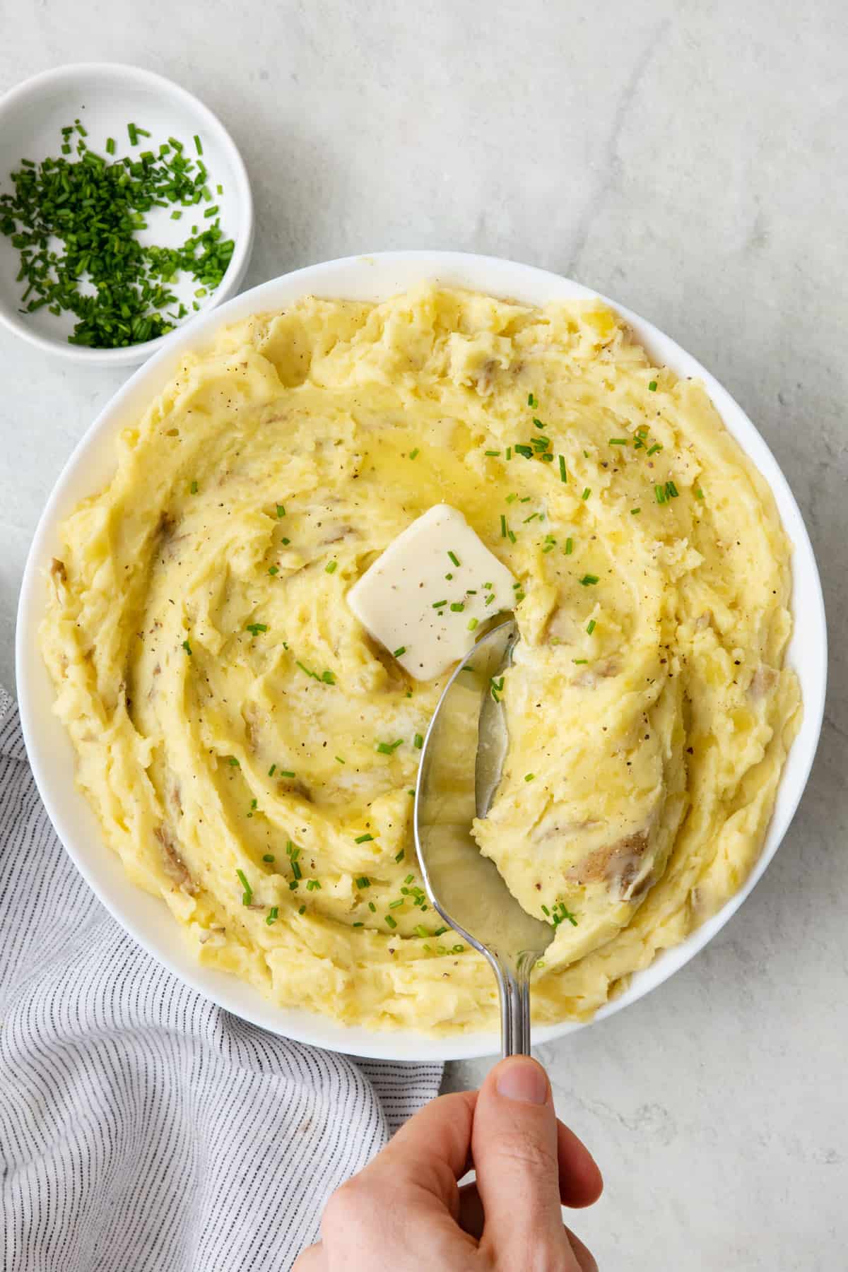 Large serving dish of garlic mashed potatoes topped with butter and herbs with a spoon scooping up some.