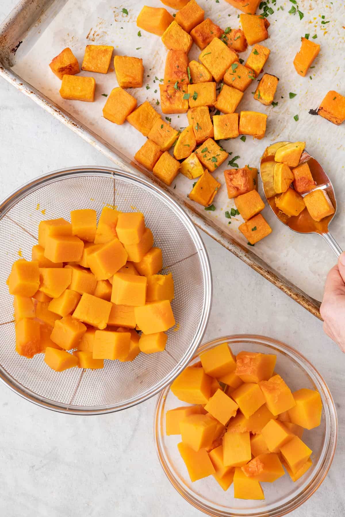 Cooked butternut squash cubes cooked three ways: roasted on a baking sheet, boiled in a strainer, and microwaved in a bowl.