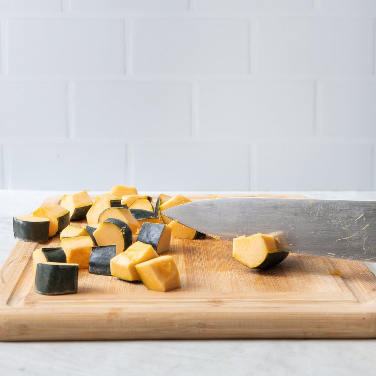 A few wedges on cutting board, most of them cut into cubes, cutting last few.
