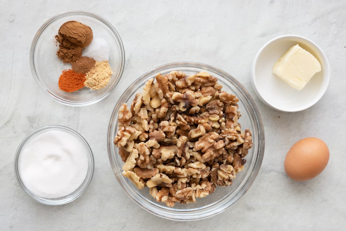 Ingredients for recipe in individual bowls: spices, sugar, walnuts, butter, and an egg.