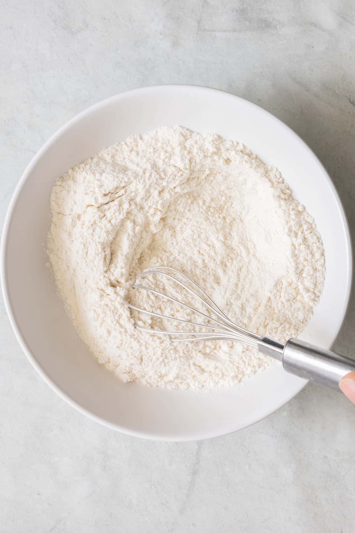 Whisking flour with baking powder and salt in a small white bowl.