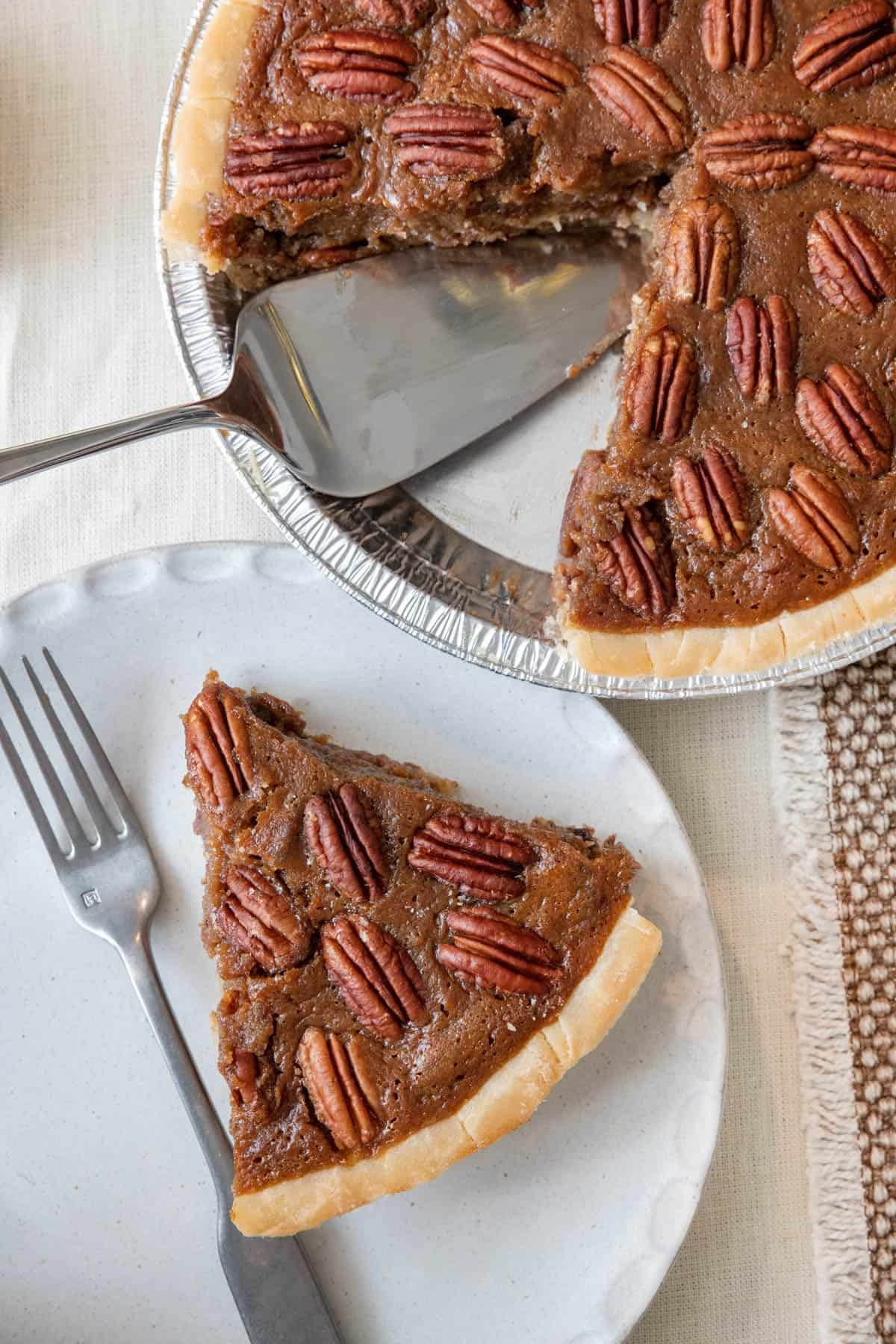 Pecan pie with a slice removed and on a small plate with a fork .