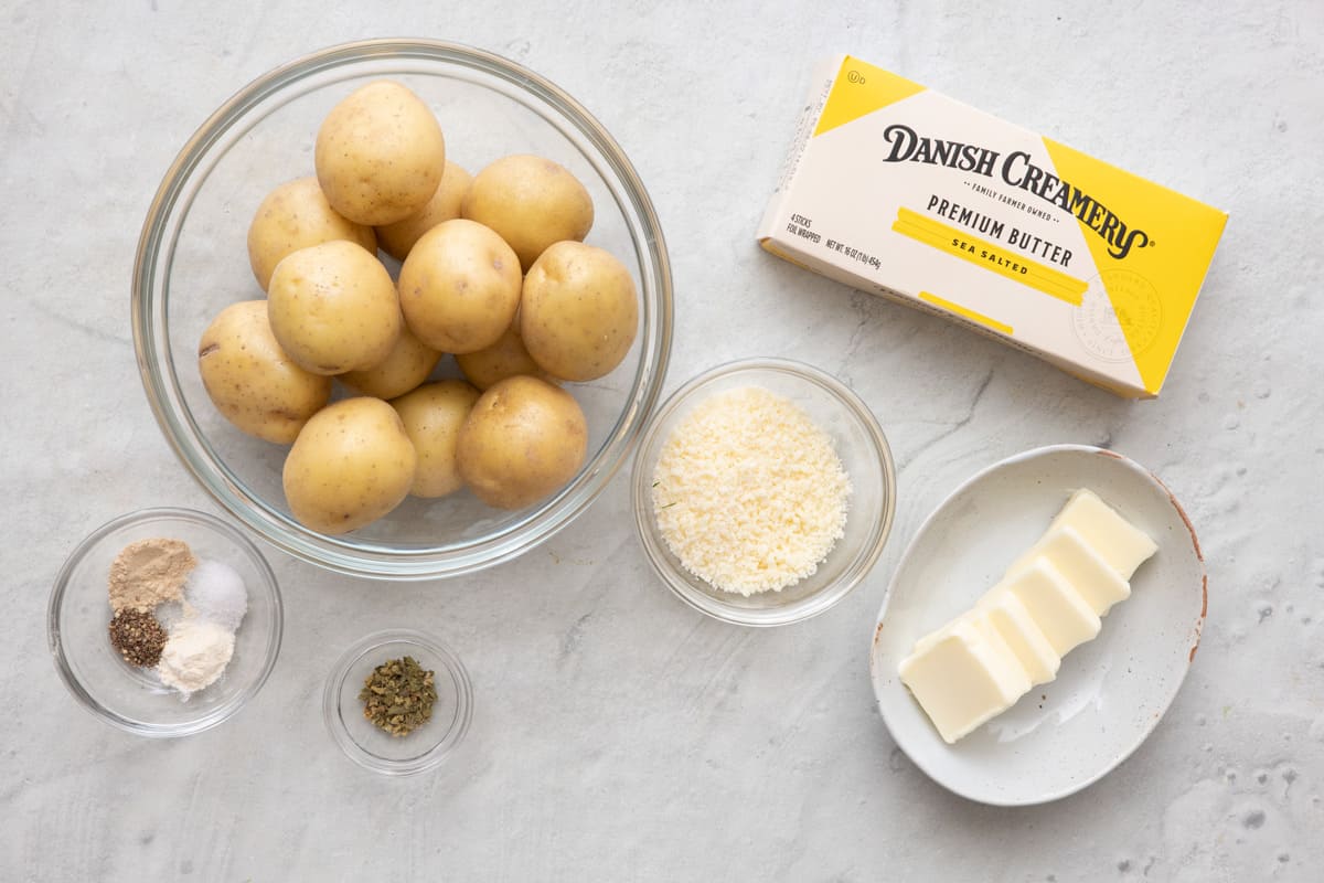 Ingredients for recipe: spices, herbs, and parmesan in indivdual pinch bowls, a bowl of small potatoes, box of Sea Salted Danish Creamery Premium Butter with some butter cubes in a small dish.