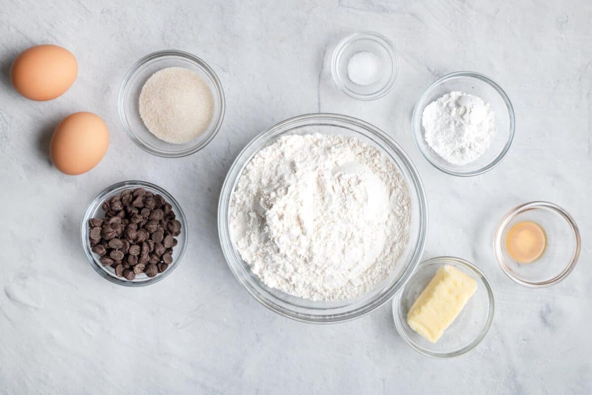 Ingredients for recipe before being prepped and in invidivdual dishes: 2 eggs, cane sugar, chocolate chips, flour, salt, baking powder, vanilla, and stick butter.