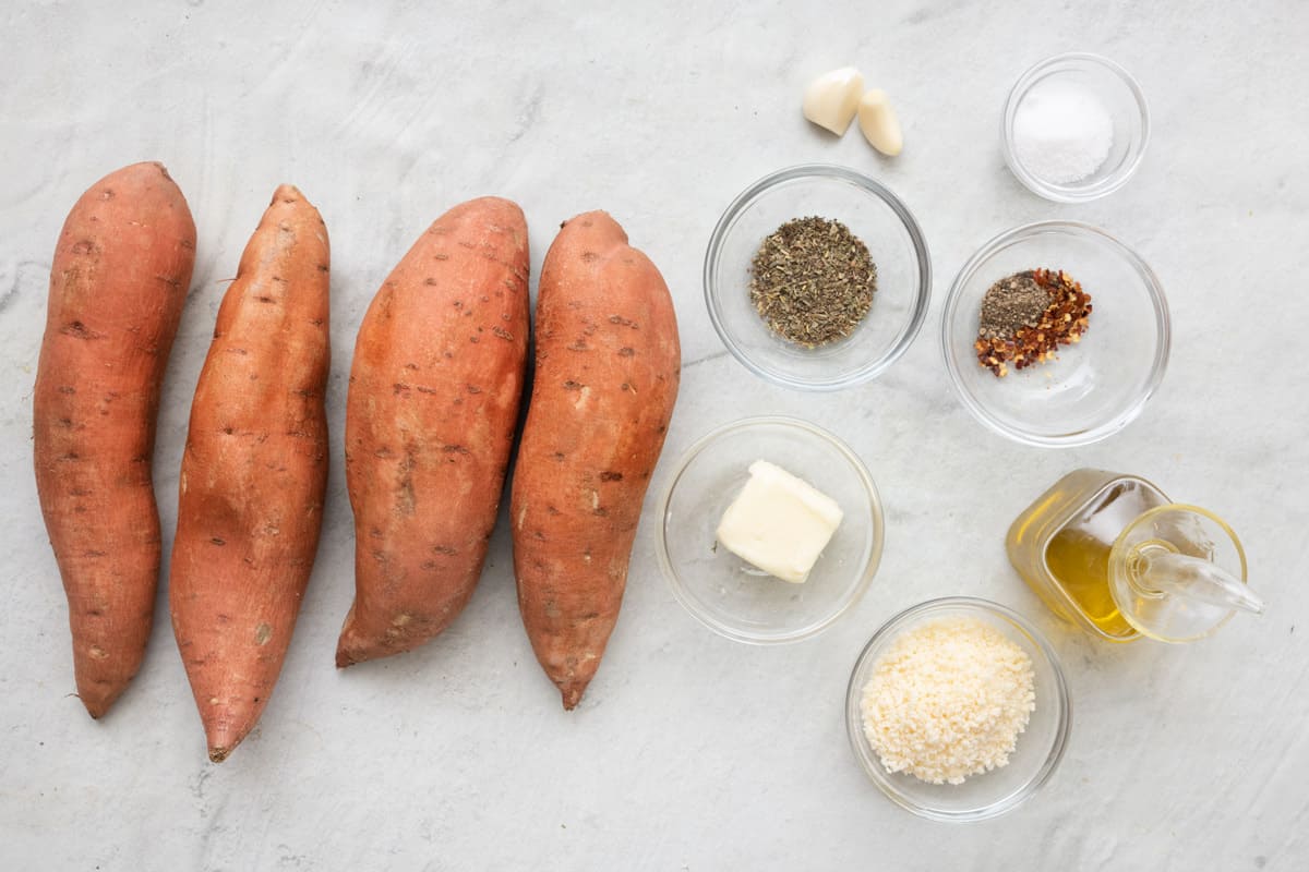 Ingredients for recipe: 4 long sweet potatoes, seasonings, garlic cloves, salt, butter, parmesan, and oil.