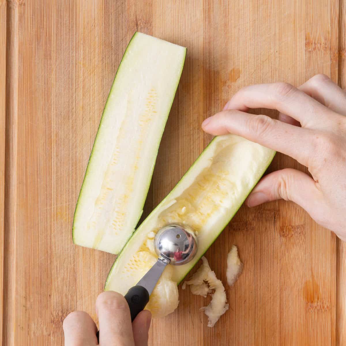 Melon scooper scooping out flesh of zucchini.