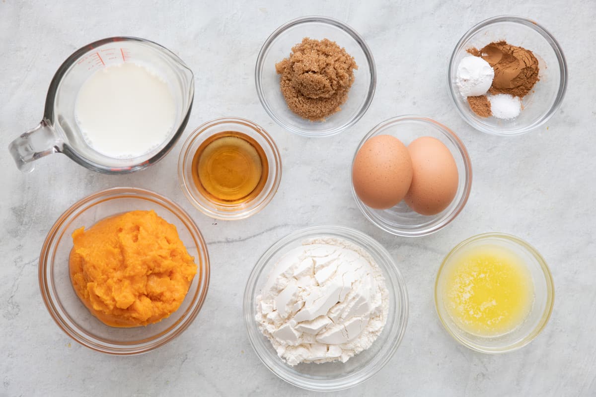 Ingredients for recipe in individual bowls: milk, mashed sweet potatoes, vanilla, brown sugar, flour, 2 eggs, seasonings, and melted butter.