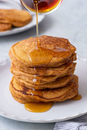 Stack of 6 big fluffy sweet potato pancakes with syrup being poured over them.