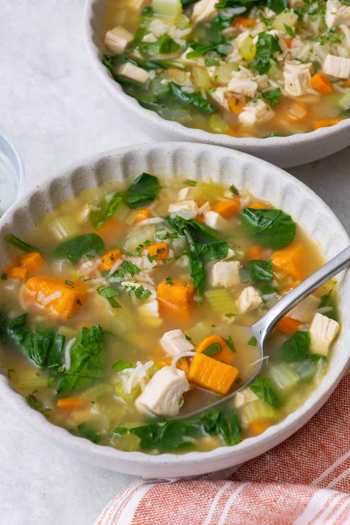 Close up of one bowl of turkey rice soup with a spoon dipped in and another bowl nearby.