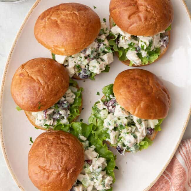 Turkey salad sandwiches on a platter with with bun lids set off to the side slightly to show salad and leafy lettuce on each one.
