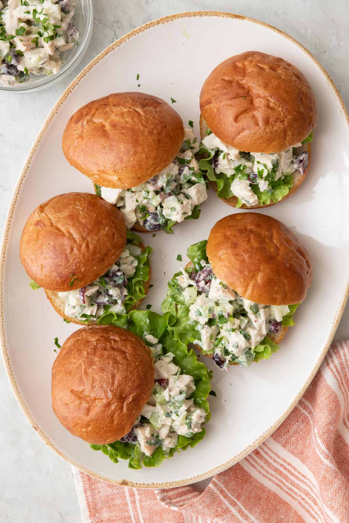 Turkey salad sandwiches on a platter with with bun lids set off to the side slightly to show salad and leafy lettuce on each one.