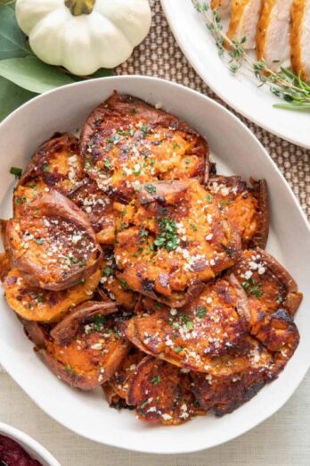 Sweet potato rounds garnished with parsley and parmesan in a serving dish with turkey slices and cranberry sauce nearby.