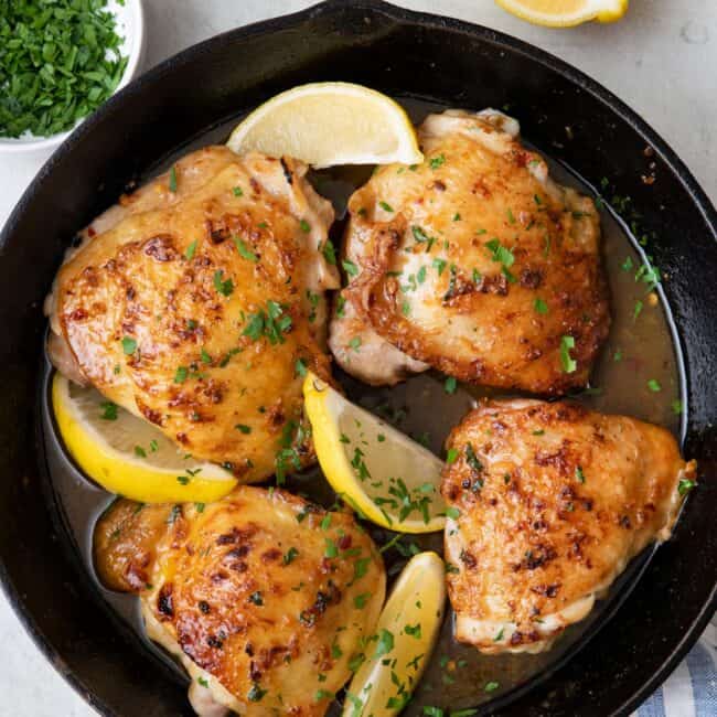 4 chicken thighs cooked in a cast iron skillet with a honey butter sauce and garnished with fresh herbs and lemon.