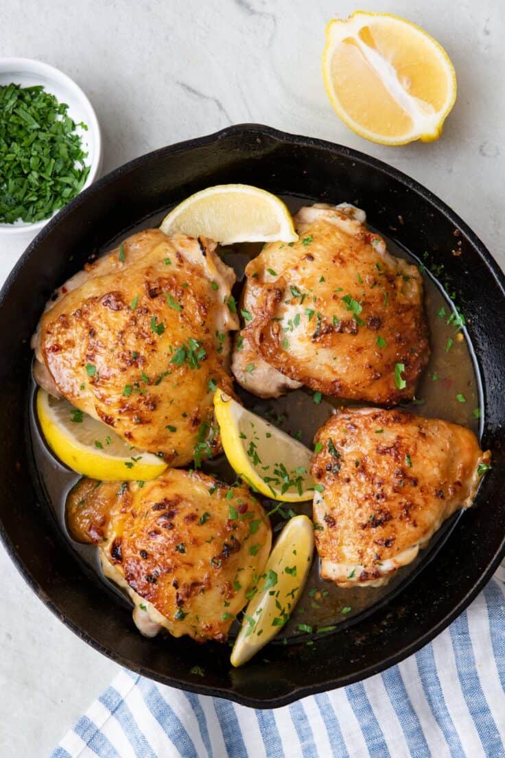 4 chicken thighs cooked in a cast iron skillet with a honey butter sauce and garnished with fresh herbs and lemon.
