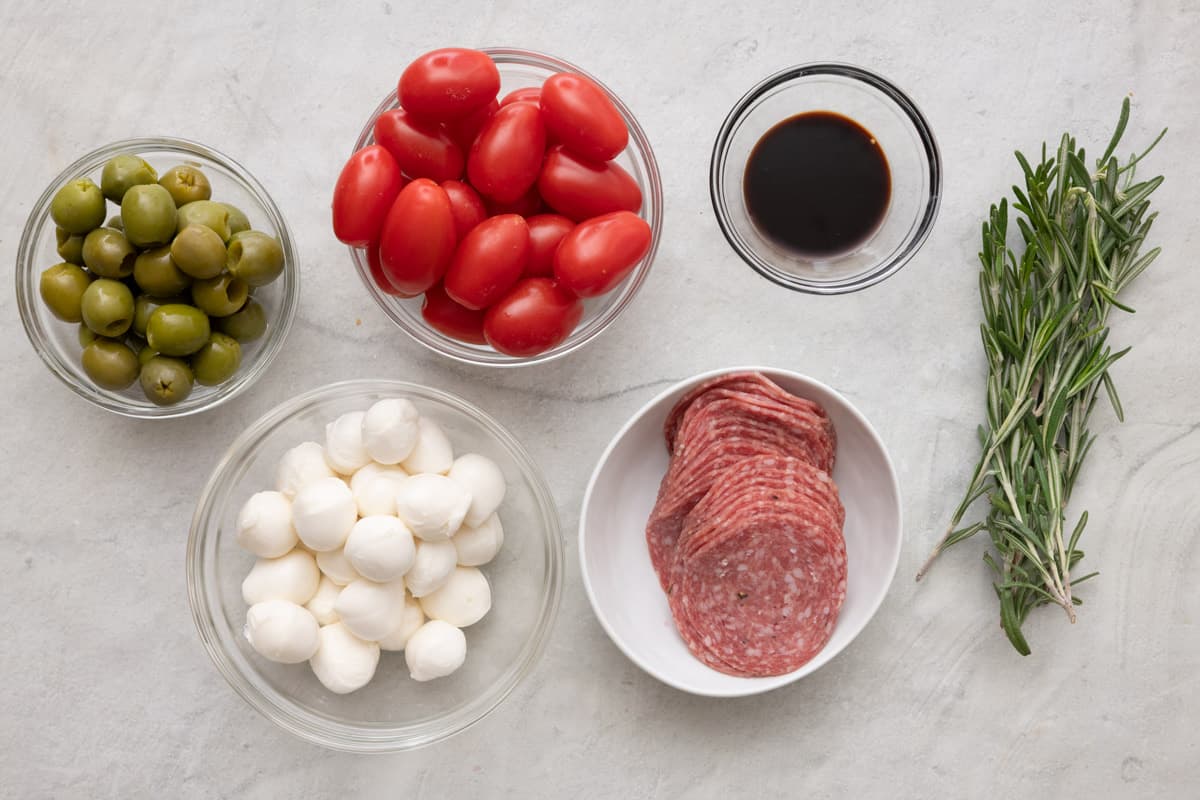 Ingredients for recipe: green olives, mozzerella balls, grape tomatoes, salami slices, balsamic glaze, and fresh rosemary sprigs.