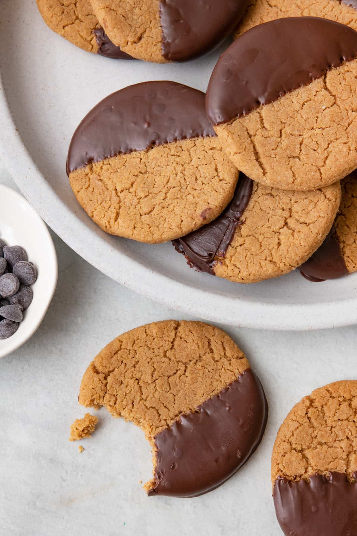 Plate of cookies with one cookie on table with bite taken out in the middle of where the chocolate is dipped.