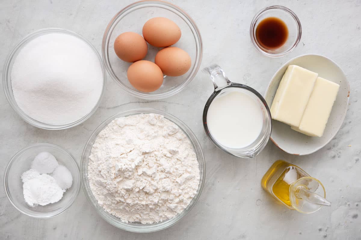 Ingredients for recipe in indiviual bowls and containers before mixed: sugar, baking powder, salt and baking powder, 4 eggs, flour, milk, vanilla, butter sticks, and oil.