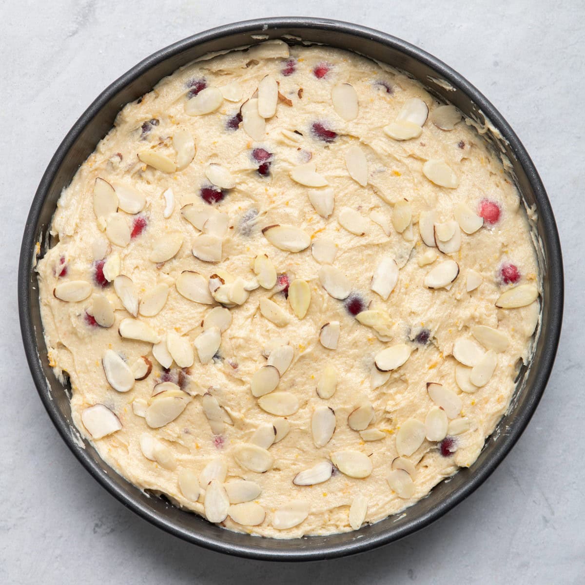 Cake batter in round pan before baking with sliced almonds on top.
