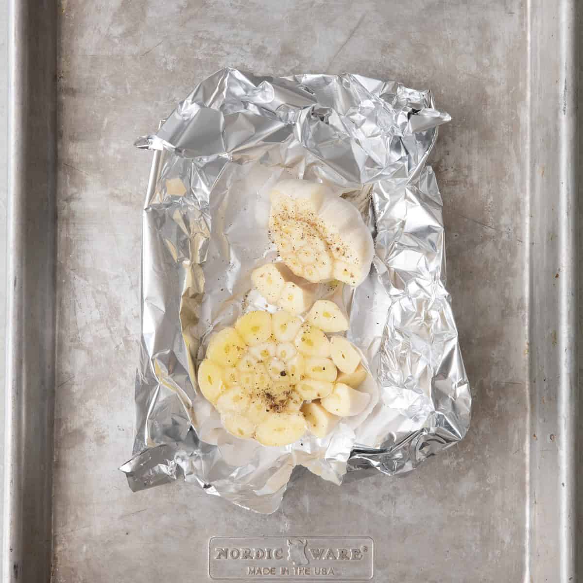 Head of garlic cut in half lengthwise with oil and seasoning in foil before being roasted.