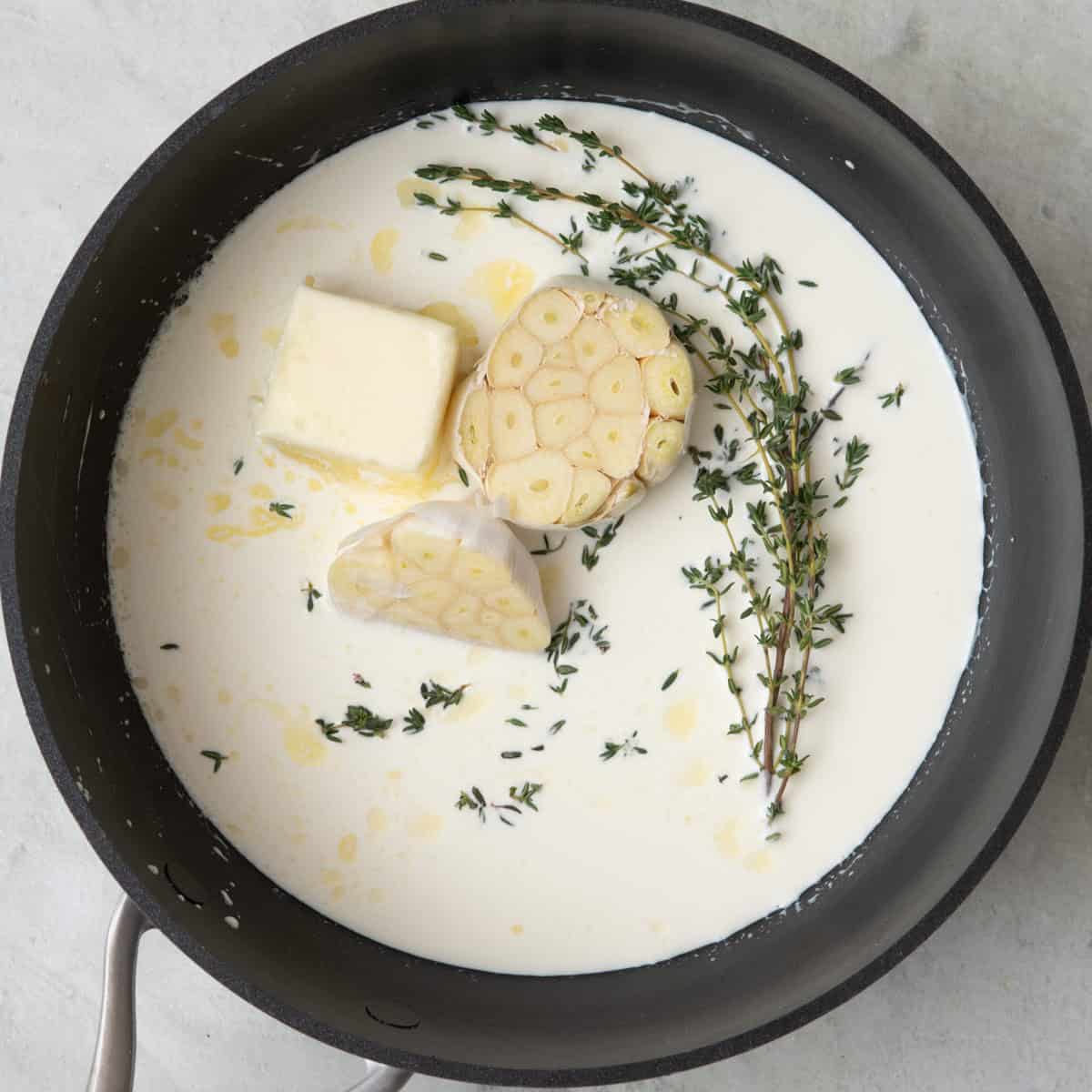 Small saucepan with another halved garlic head (not roasted), cream, butter, and thyme before mixed.