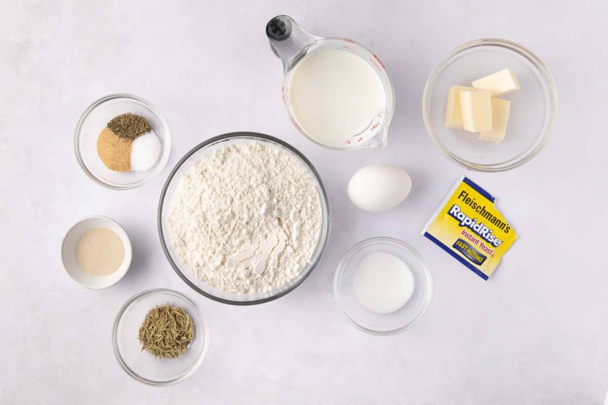 Ingredients for recipe in individual bowls: garlic powder, salt, and rosemary, thyme, sugar, flour, milk, butter, an egg, and Fleischmann’s® RapidRise® Instant Yeast package with contents in a small bowl.
