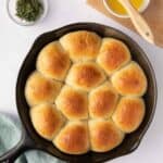 Garlic herb Skillet Dinner Rolls basted with butter in a cast iron skillet with fresh sprigs of rosemary and extra butter and brush nearby.