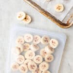 Frozen banana slices inside a reusable freezer bag with tray of them nearby.