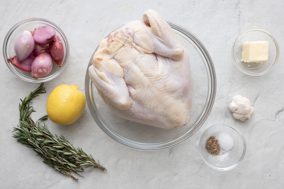 Ingredients for recipe before preppped: 6 large shallots, fresh rosemary sprigs, whole lemon, whole chicken, butter, head of garlic, salt and pepper.
