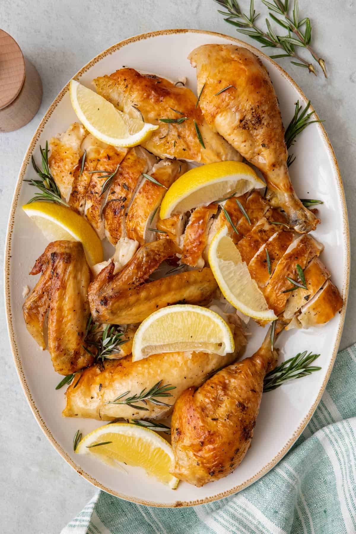 Roasted chicken broken down into thighs, wings, legs, and sliced breast displayed on a platter with fresh rosemary and lemon slices or wedges.