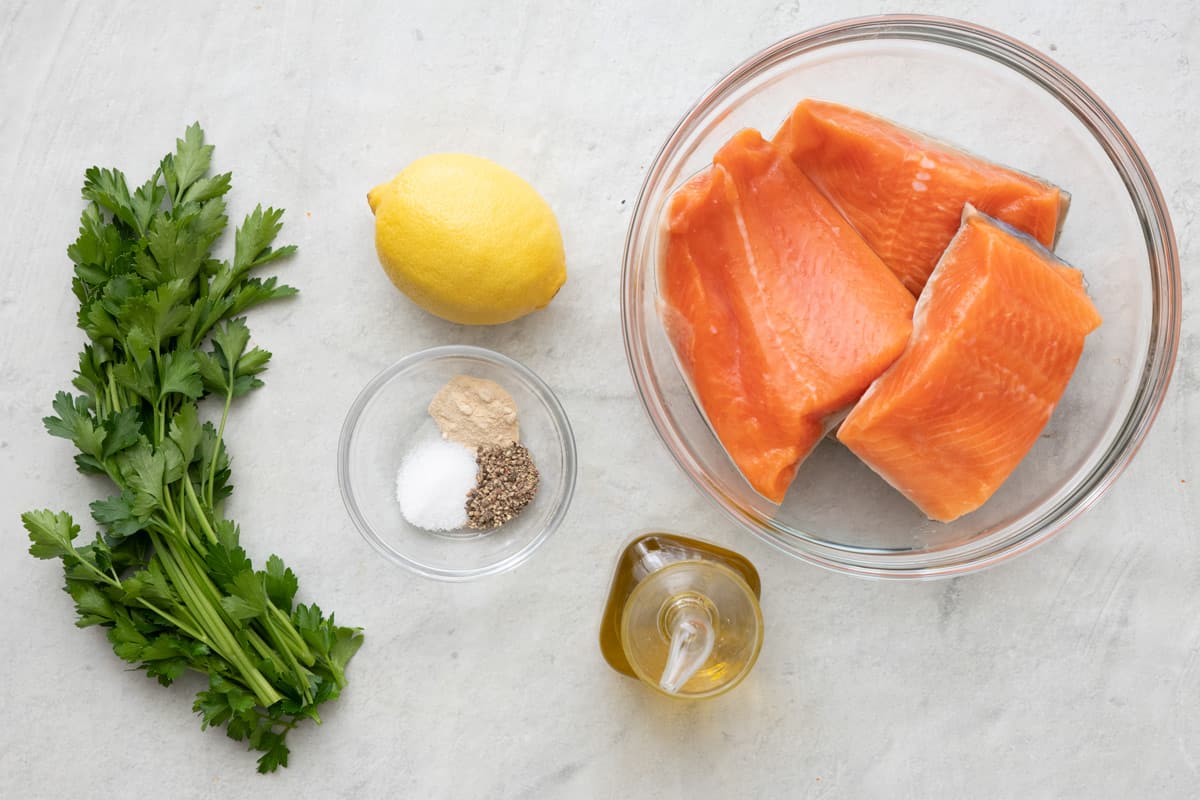 Ingredients for recipe: fresh parsley (for serving), lemon, spices, salmon filets, and oil.