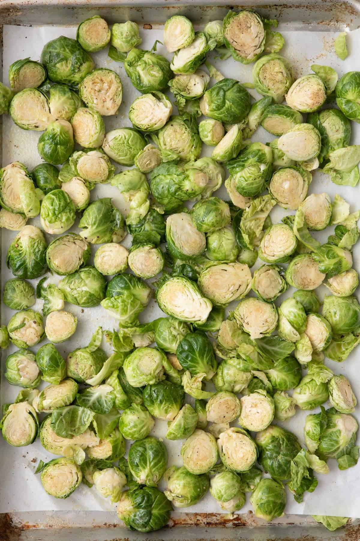 Brussels sprouts on a parchment lined baking sheet tossed with oil and seasoning before baked.