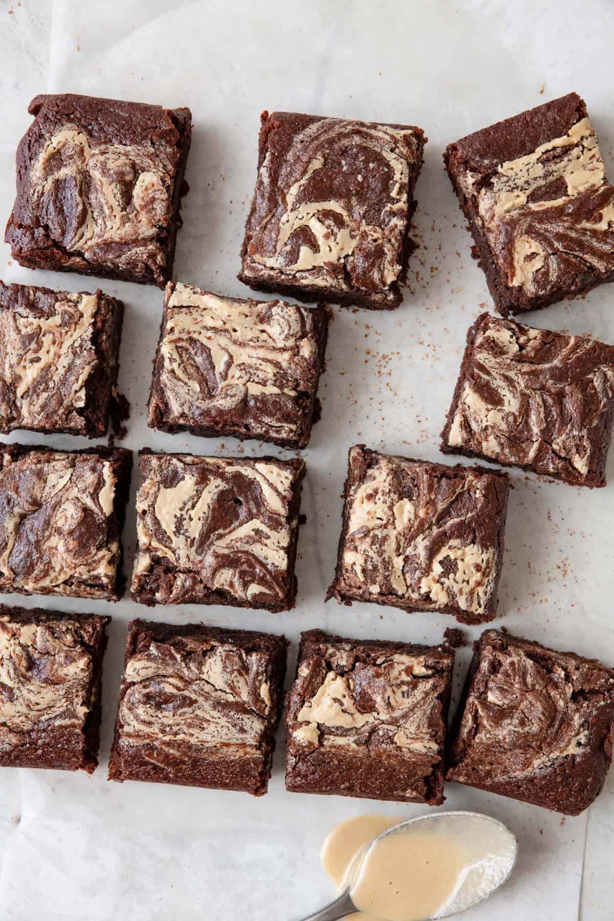 Tahini swirled brown squares set off line from cutting and a spoon with tahini on it nearby.