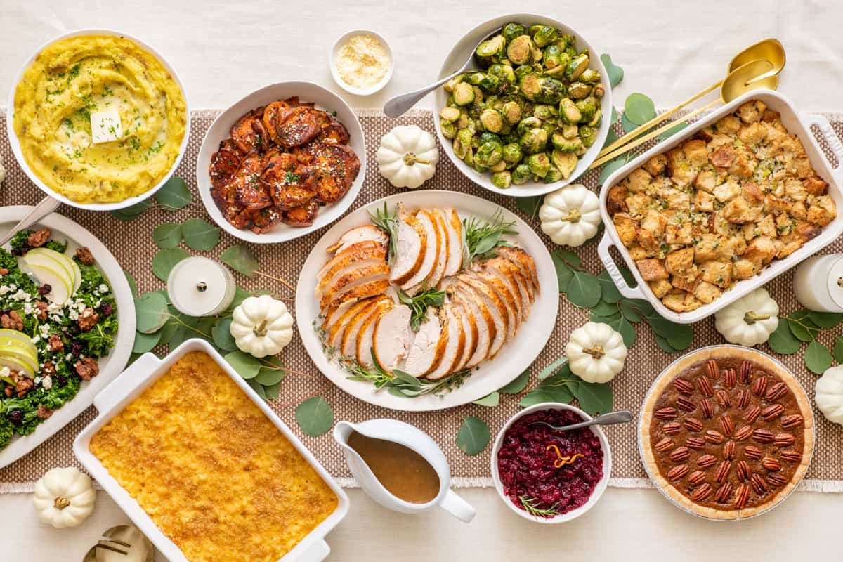 Ovehead shot of a full Thanksgiving table with various side dishes and sliced turkey breast.