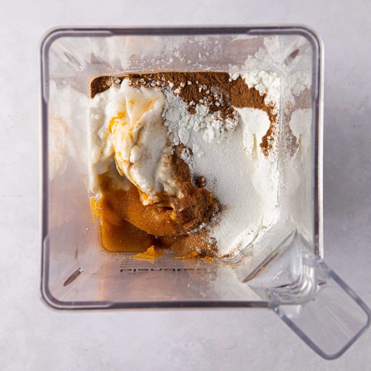 Blender filled with pumpkin puree, corn starch, coconut cream, vanilla, sugar, salt and spices before blending and making the vegan pumpkin pie filling.