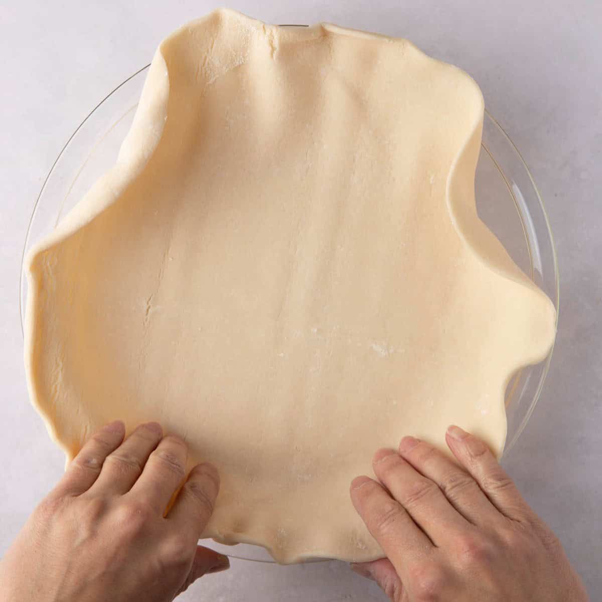 Two hands pressing the vegan pumpkin pie crust into a pie dish.