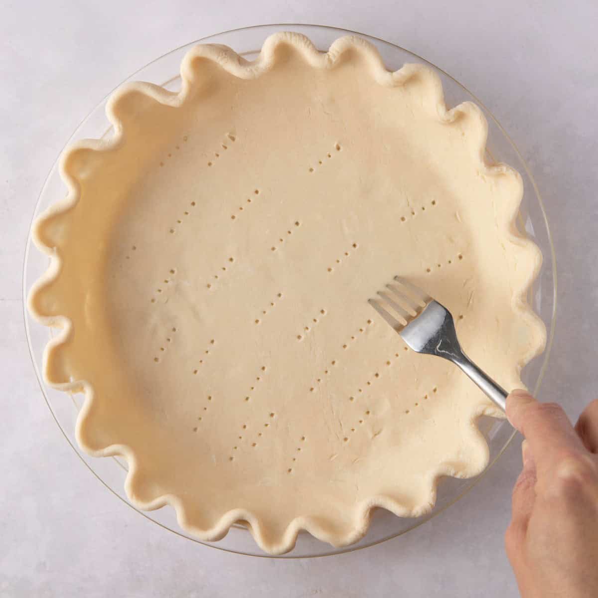 A fork pricking the crust of the vegan pumpkin pie at its base.