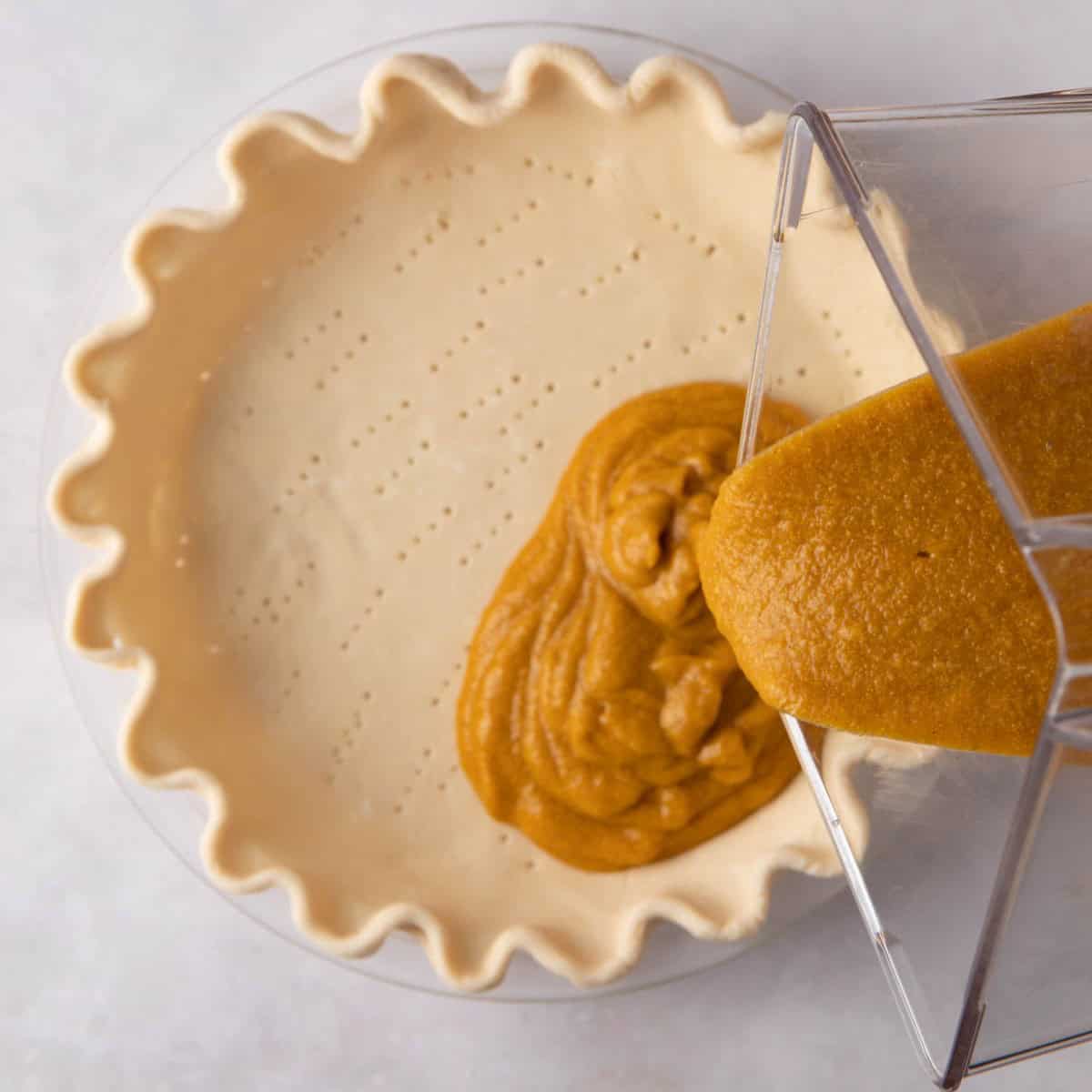 Pouring the vegan pumpkin pie filling from the blender into the crust.