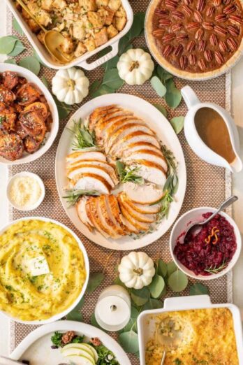 Thanksgiving table serving sliced turkey breast, smashed sweet potatoes, roasted brussel sprouts, baked mac and cheese, and gravy.