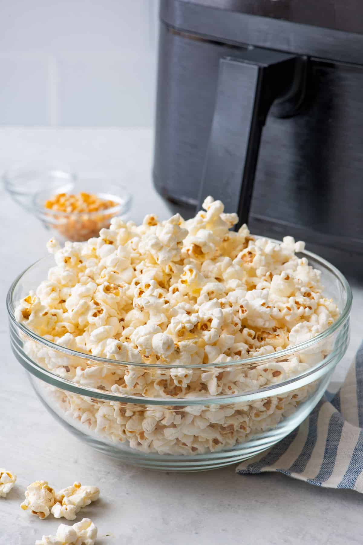 Popcorn in a serving bowl piled high with an air fryer behind it.