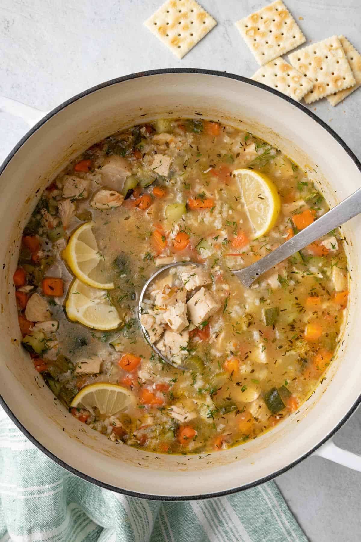 Pot of chicken vegetable soup with ladle dipped in and a few crackers on the side.