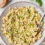 Prepared chickpea "tuna" salad in serving bowl with spoon dipped in, garnished with fresh dill and a few slices of bread nearby.
