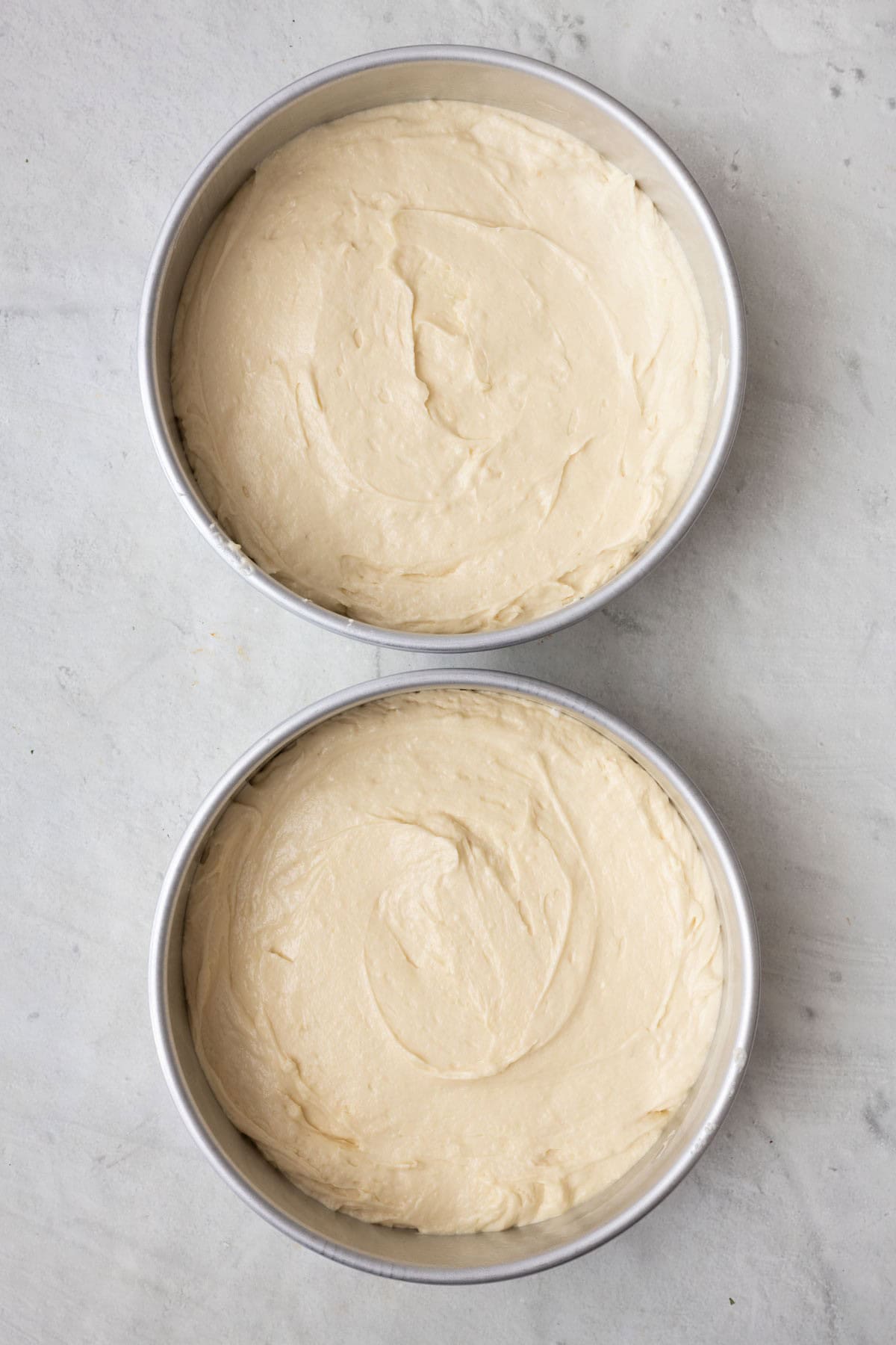 Two round cake pans lined with parchment paper filled with batter before baked.