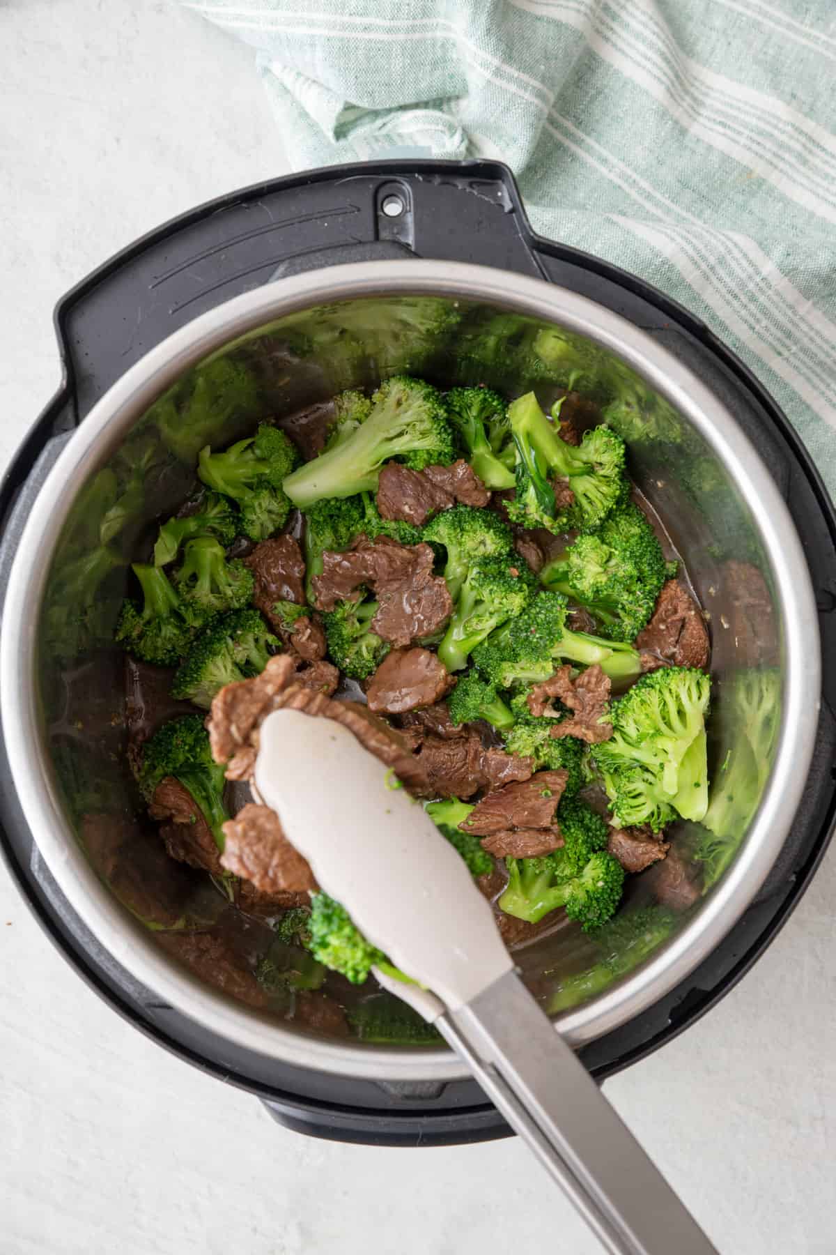 Tongs scooping up beef and broccoli from Instant Pot.