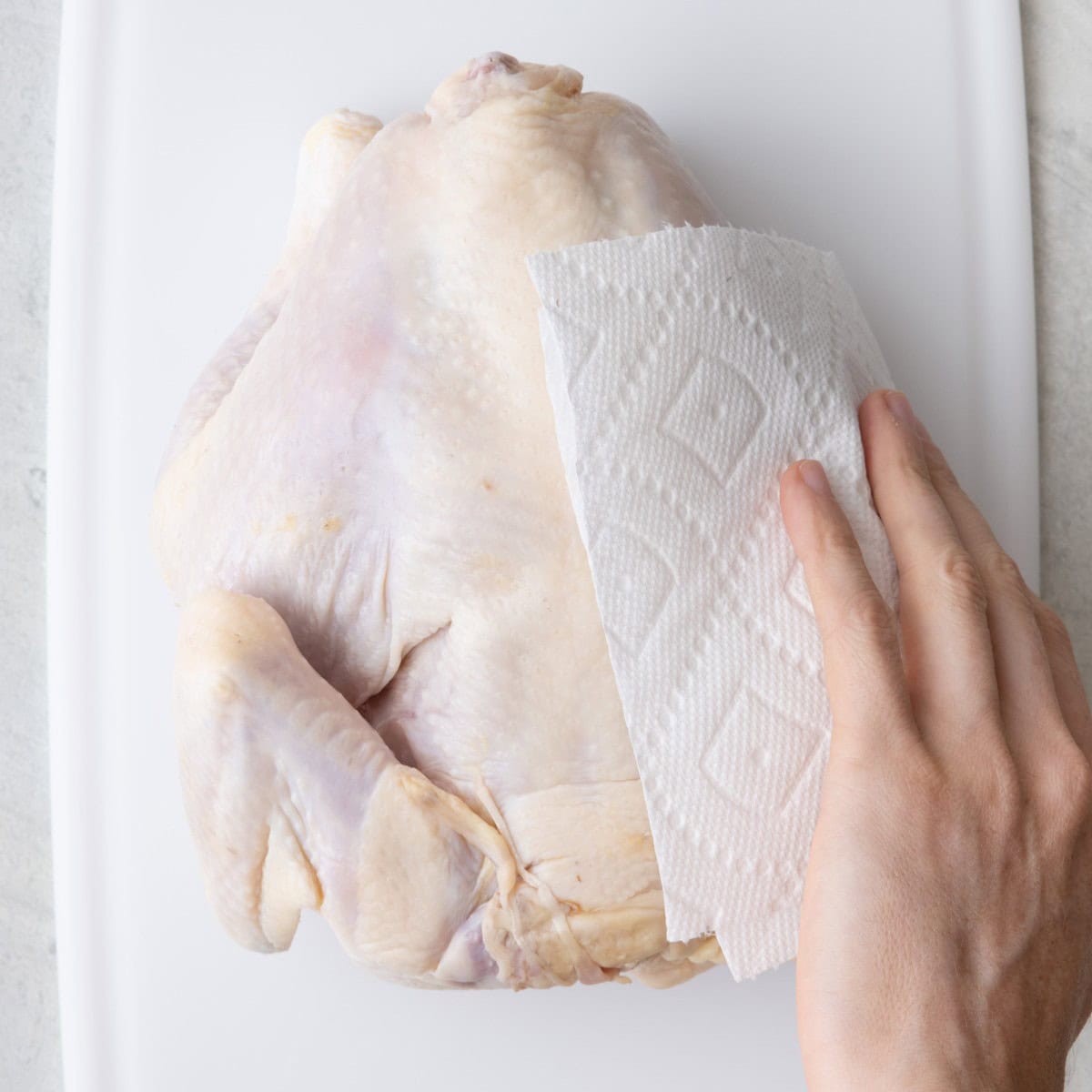 Paper towels patting dry chicken on cutting board.